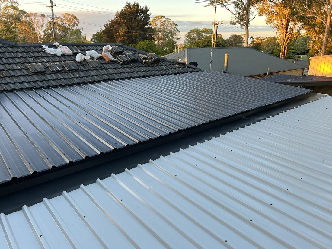 Completed grey metal roof repair beside an existing tiled roof